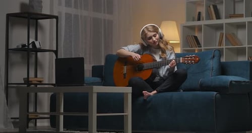 Young Woman Plays Guitar at Home in Evening