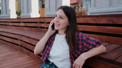 Woman Chatting on Smartphone While Sitting Outdoors