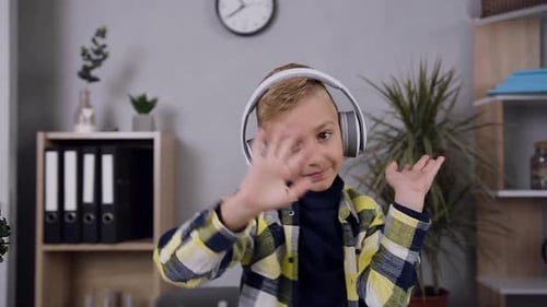 Lächelnder tanzender Teenie-Junge in Kopfhörern, der vor der Kamera in seinem
