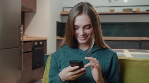 Smiling Woman Using Smartphone on Sofa Indoors