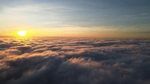 Aerial view of vibrant yellow sunrise over white dense clouds with blue sky overhead