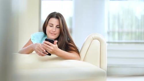 Woman Using Smartphone Relaxing on Sofa Indoors