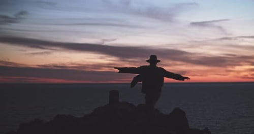 Silhouette of a man with a hat walking towards a cliff at dusk