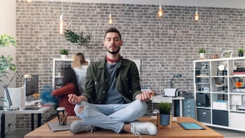 Zeitraffer eines jungen Mannes, der sich in Lotusposition auf dem Schreibtisch im Büro entspannt