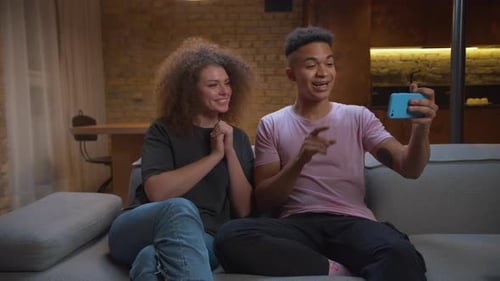 Multiethnic Bloggers Couple Recording Video on Mobile Phone Sitting on Sofa at Home
