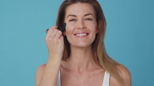 Woman Applying Makeup With Brush on Blue Background
