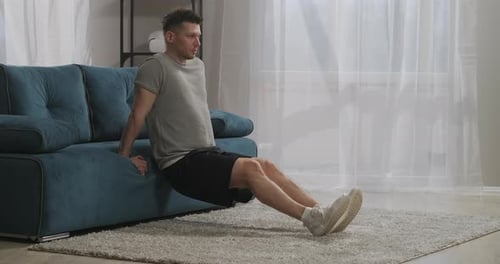 Home Fitness of Young Sporty Man Person Is Lifting His Own Weight Leaning on Couch in Living Room