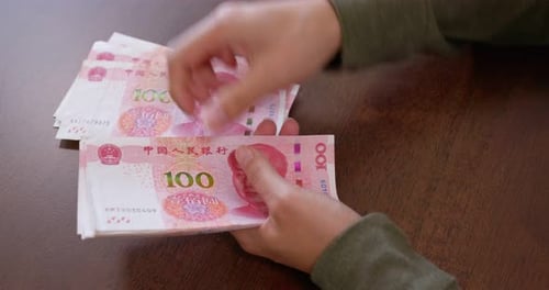 Hands Counting Stacks of Chinese Yuan