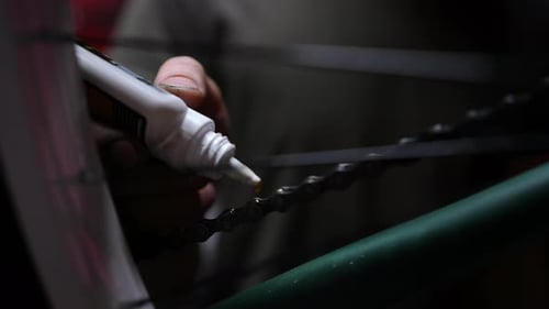 Closeup of Unrecognizable Skilled Repairman Greasing Oiling Lubricating Links of Bicycle Chain