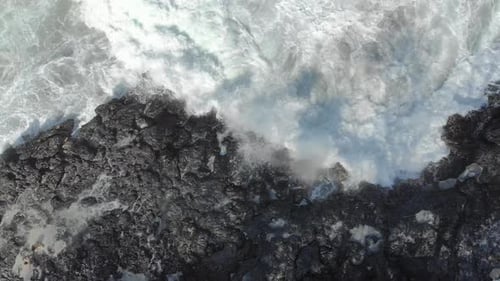 Aerial Shot of a Black Volcanic Beach. Waves Crash on the Rocks Causing the Appearance of a Natural