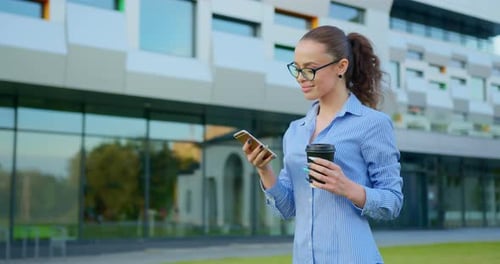 Woman Walks with Phone and Coffee Near Office