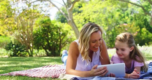 Happy mother and daughter using digital tablet in park 4k