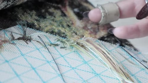 Woman hands doing cross-stitch of green nature.