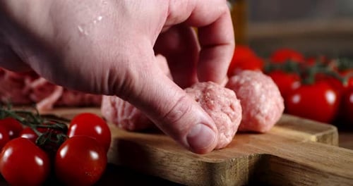 Hand Placing Raw Meatball on Wooden Cutting Board