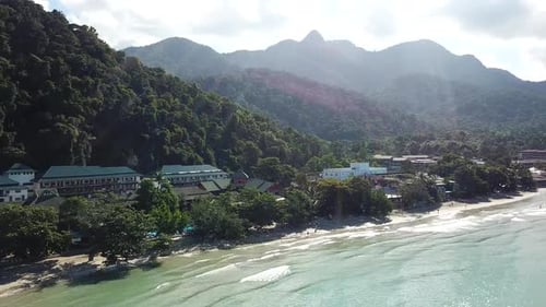 The green hills of the island are covered with palm trees, the sky is cloudy