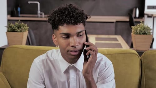 Young Man Chatting on Smartphone on Couch Indoors
