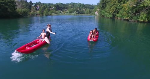 Four friends having fun paddling canoe and jumping into river