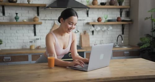 Woman Typing on Laptop and Drinking Juice at Home