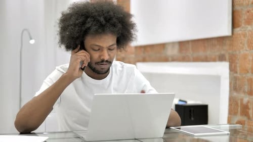 Young Adult Talking on Phone Using Laptop