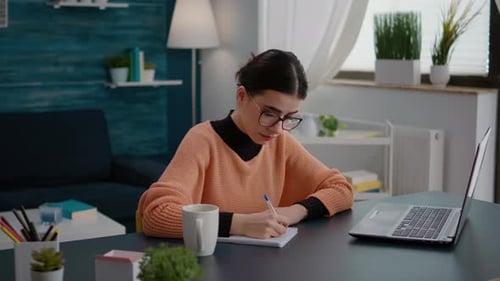 Woman Writing in Notebook at Desk at Home