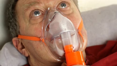 Homme malade d'âge moyen respirant lourdement à travers un masque à oxygène roulant ses yeux couché dans son lit