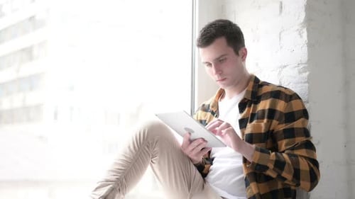 Young Man Using Tablet While Sitting by Window