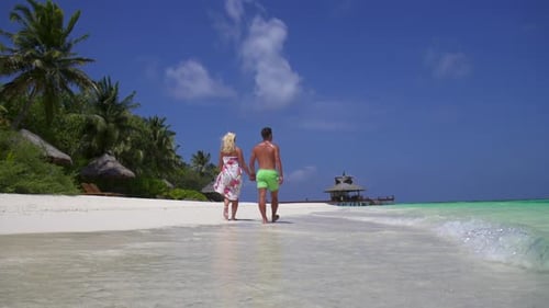 A couple walks on the beach holding hands at a tropical island resort hotel