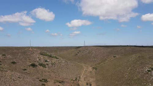 Drone Flying Over Field with Clouds Hovering Above and Electric Pylons Seen in Background