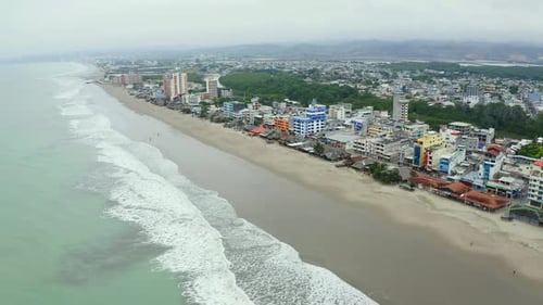 Vista aérea circulando sobre o oceano ao lado de uma cidade ao lado de uma praia no Equador