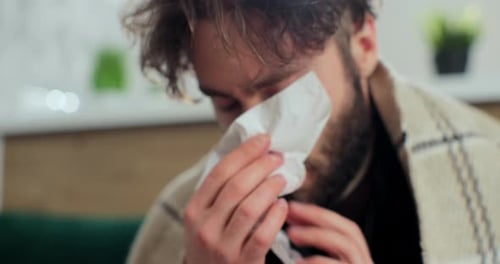 Close Up of the Young Sick Man in the Warm Scarf and a Plaid Blowing His Nose in the Napkin As He