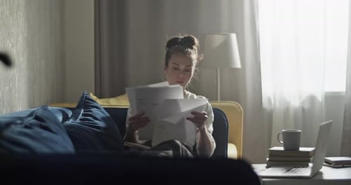 Woman Reads Through Documents on Sofa
