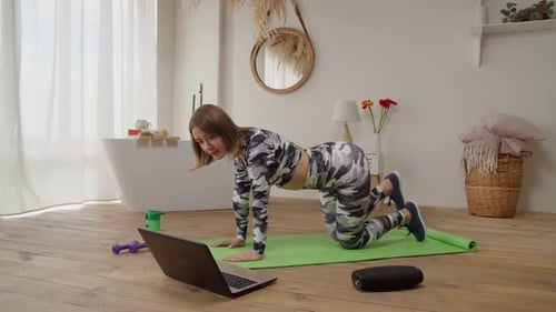 Encantadora mujer en forma deportiva viendo un Vídeo tutorial en una computadora portátil haciendo ejercicio de yoga con patada de burro en casa