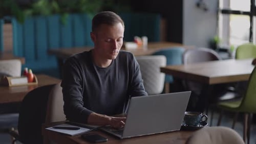 Handsome Freelancer Businessman in Glasses Diligently Working on Laptop in Cafe