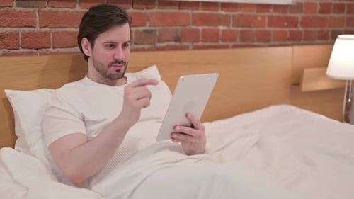 Man Relaxing in Bed Using Tablet