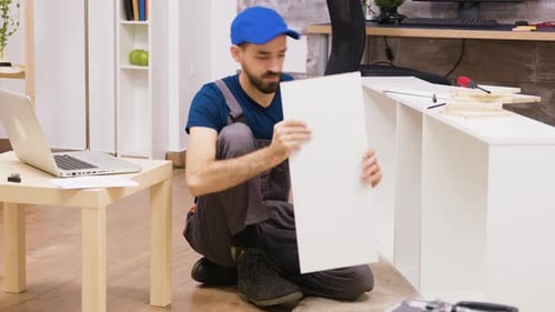 Man Assembling White Bookshelf Using Laptop Instructions