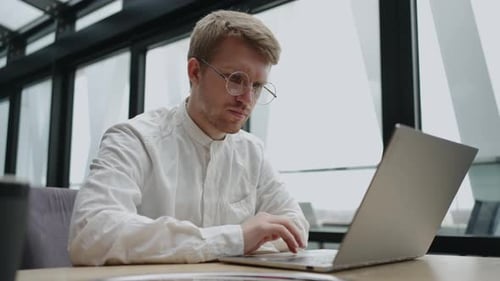 Concentrated Young Man Typing on Laptop in Cafe