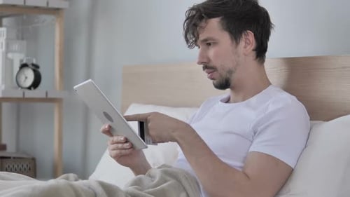 Man Using Tablet, Credit Card in Bedroom