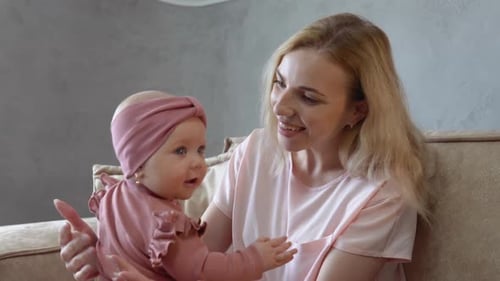 Baby Girl with Blue Eyes in a Cute Pink Suit Playing with Mom on Her Lap