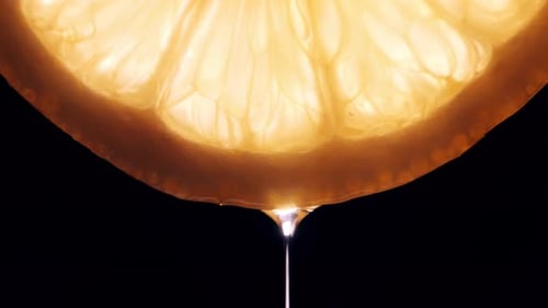 Ein Tropfen Saft fließt von einer Zitronenscheibe auf schwarzem Hintergrund in Makro