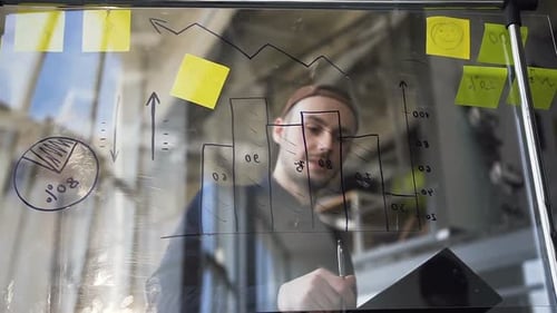 Junger Geschäftsmann in Freizeitkleidung mit Glasplatte mit Diagramm bei Berechnungen