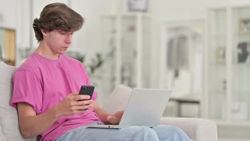 Young Adult Using Smartphone and Laptop on Sofa