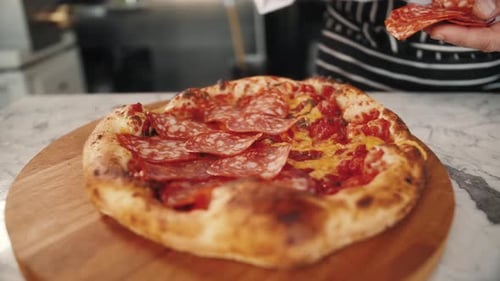 Chef Adding Pepperoni to Pizza in Kitchen