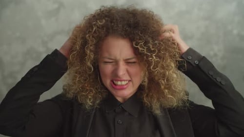 Jolie femme irritée aux cheveux bouclés à la recherche d'une expression furieuse à l'intérieur