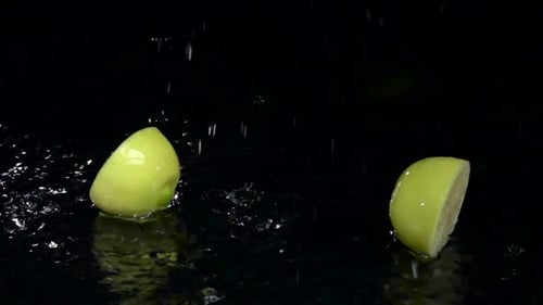 Lemon Falls Into the Water and Breaks Up Into Two Parts. Black Background. Slow Motion