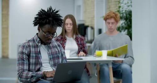 Absorbed African American Office Worker Typing on Laptop Keyboard, Looking at Camera and Smiling