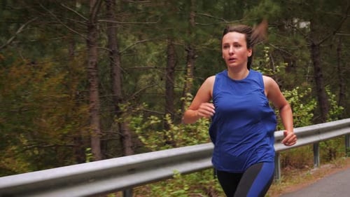 Woman Runs Through a Forest on a Winding Road