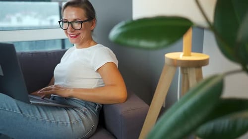 Smiling Woman Using Laptop on Couch at Home