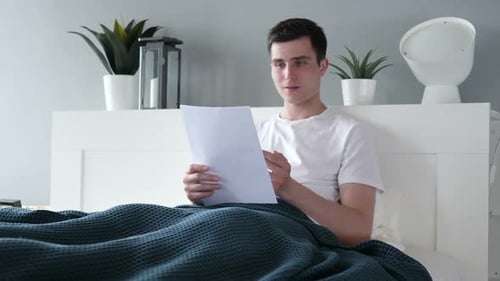 Man Reading Good News in Bed, Smiling