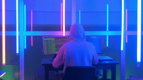 Vue arrière à moyenne distance d'un hacker criminel travaillant le soir sur un ordinateur dans un grand bureau