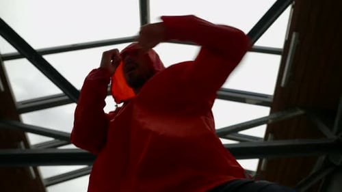 a Man in a Red Jacket with a Hood is Boxing Against the Background of Iron Structures